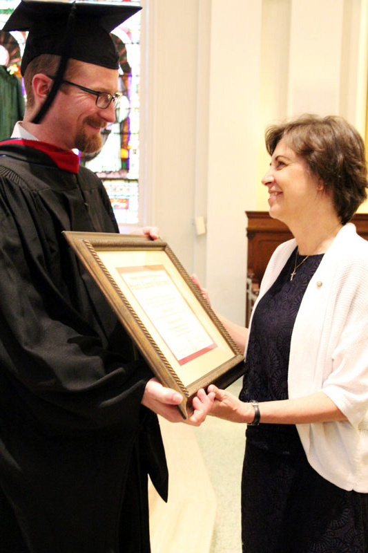 Jared Hasslebarth presents the posthumous degree to Paula Miola for her husband Steven R. Miola who recently passed away