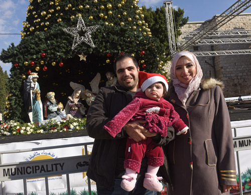 Muslim Palestinian Ashraf Natsheh, 28, holds his daughter Lara, 10 months, next to his wife, Shahad, 26, in front of the Christmas tree in Manger Square Dec. 5 in Bethlehem, West Bank. They had been unable to get into Bethlehem last year. (CNS photo/Debbie Hill) 