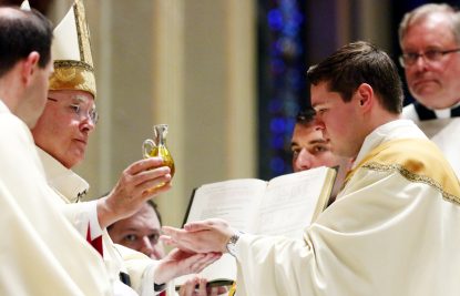 Archbishop Chaput pours the oil of sacred chrism into the hands of Father Matthew Brody.