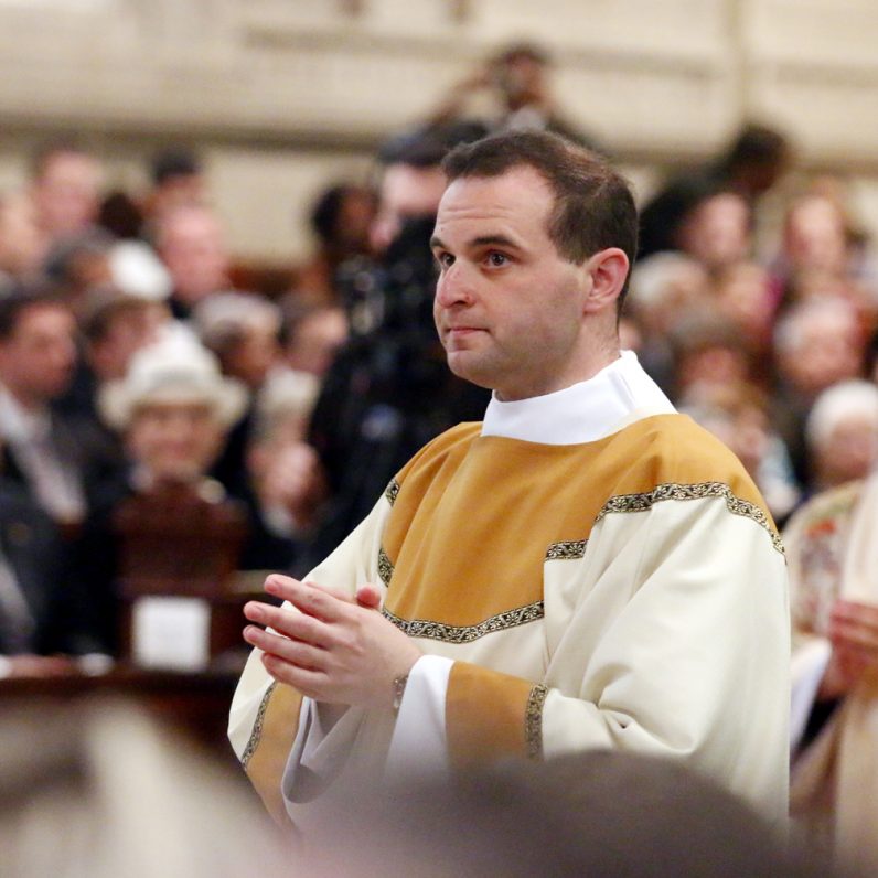 Transitional Deacon Eric Banecker wears the dalmatic, the outer liturgical vestment of a deacon, for the first time as he prays during the ordination rite.